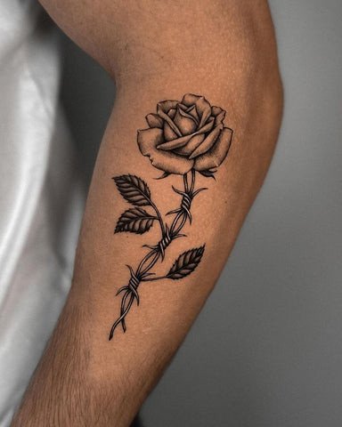 Black rose tattoo on a forearm with delicate line work and subtle gray shading, conveying a sense of mystery and elegance.