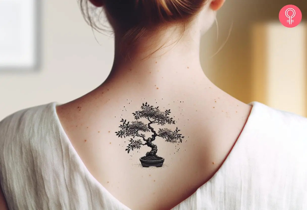 A woman's upper back features a small, minimalist black bonsai tree tattoo, subtly making a statement of elegance and tranquility.