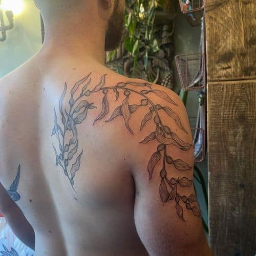 Two botanical tattoos on men, one on the forearm with a realistic botanical flower and another on the arm with a minimalist leaf outline.