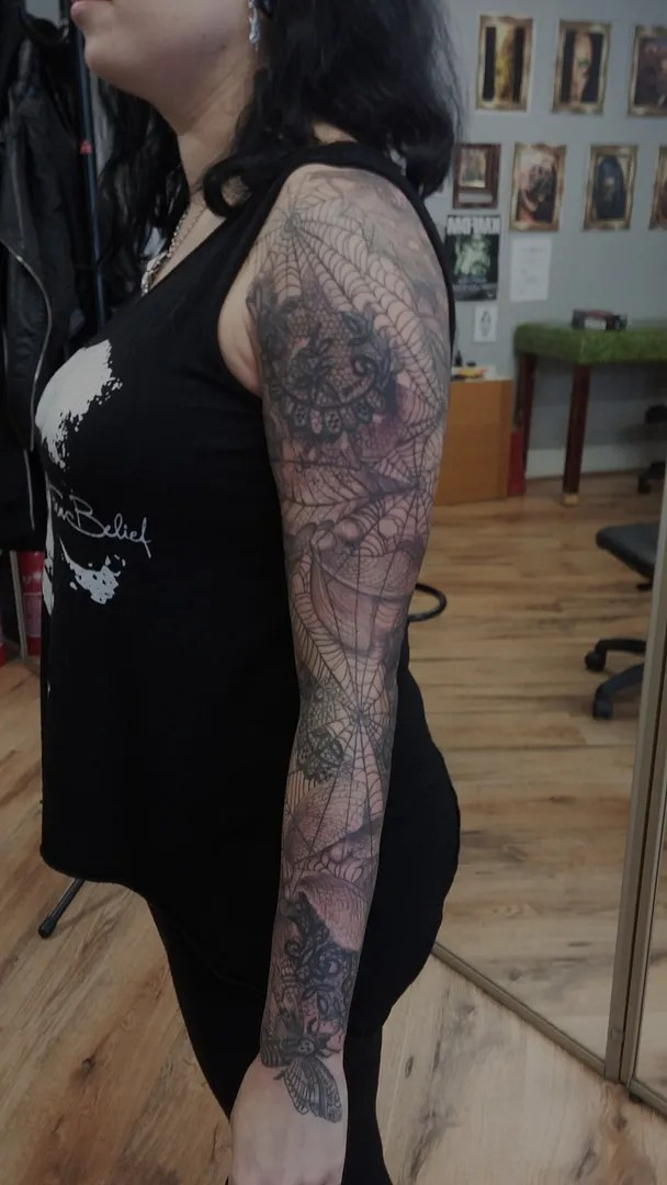 Close-up of the detailed cobweb tattoo with insects and lace elements