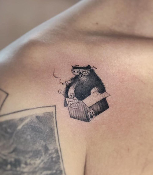 A humorous tattoo of a chubby cat with glasses, smoking and lounging in a cardboard box, showcasing a playful and quirky design.