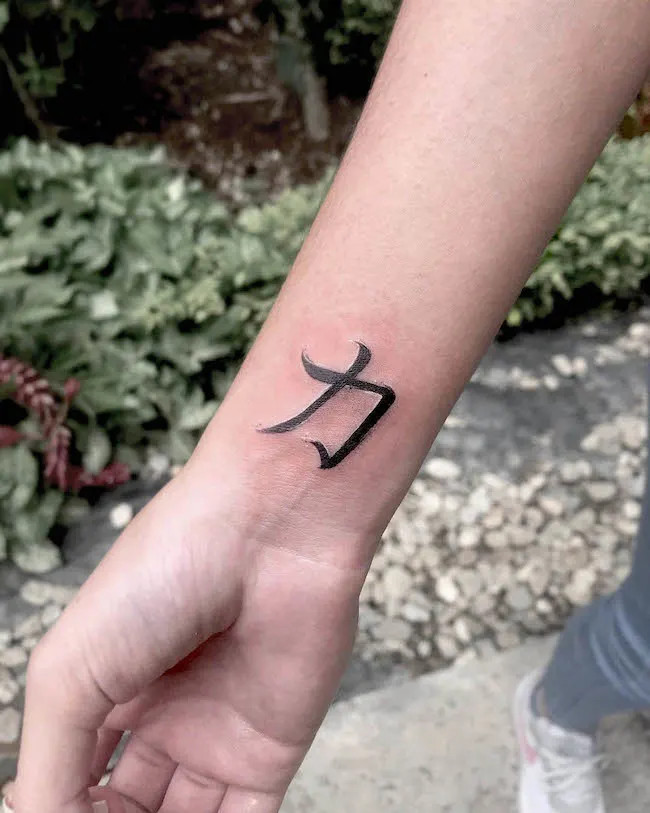 alt text: Chinese character for &quot;strength&quot; 力 tattoo on wrist in black ink, symbolizing power and perseverance rooted in Eastern culture