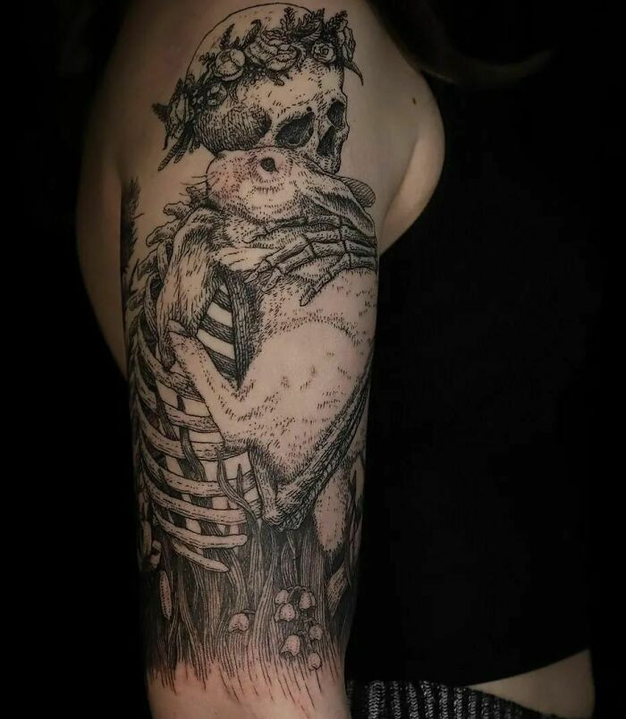 Gothic tattoo of a skull adorned with flowers and a rabbit, showcasing intricate detail and symbolism on an arm.