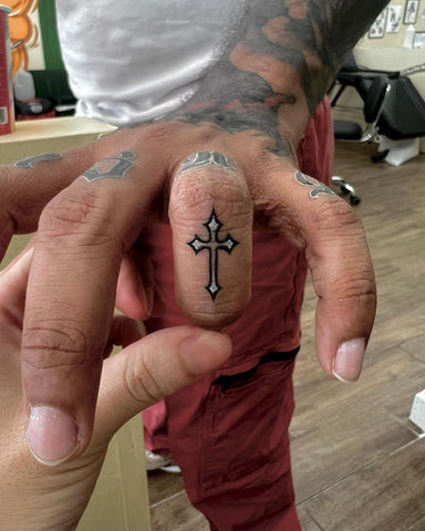 Tiny black ink cross tattoo on a man's finger, minimalist and discreet.