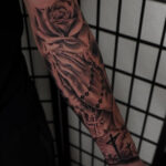 Detailed cross tattoo on a man's upper arm, showcasing intricate linework and shading.