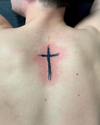 Large detailed cross tattoo on a man's upper back, expansive and intricate design.