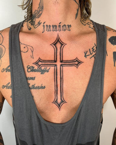 Ornate cross tattoo on a man's chest, featuring decorative elements and elaborate linework.