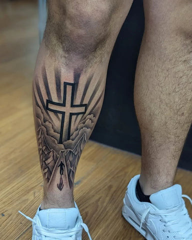 Simple black cross tattoo on a man's thigh, minimalist and understated design.