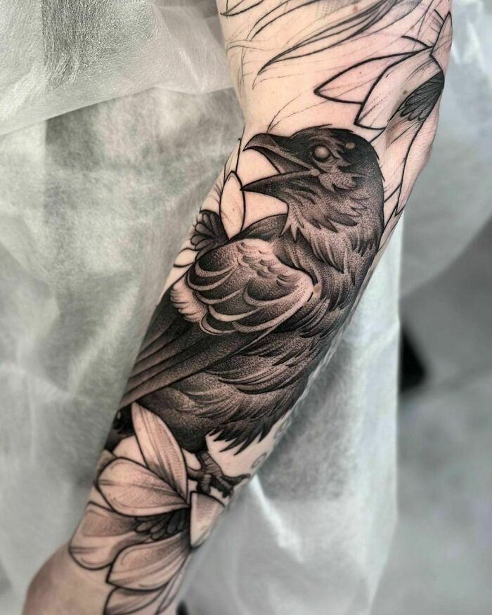 Close-up gothic tattoo of a detailed raven design on an arm, emphasizing intricate feather details and a somber atmosphere.