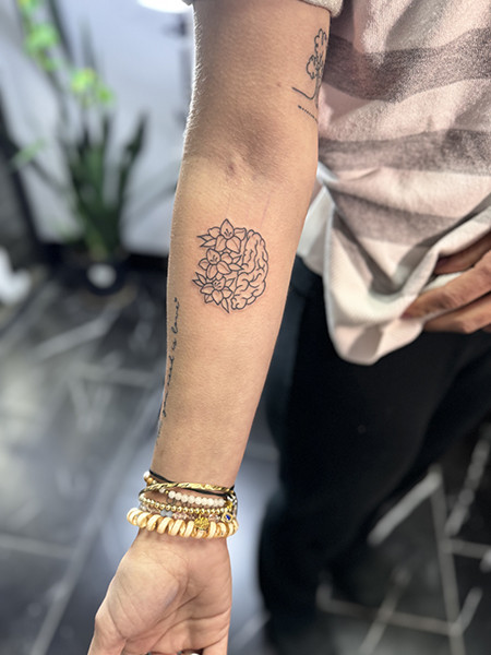 A unique half-brain, half-flower tattoo in black ink on Danielle's forearm, symbolizing strength and resilience against glioblastoma.