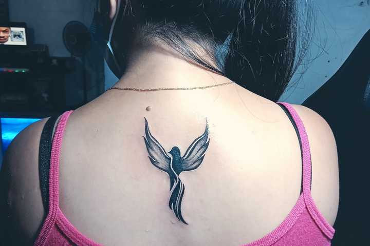 A small and delicate phoenix tattoo on a woman's back, showcasing fine linework for a subtle yet impactful symbol of rebirth, resilience, and understated feminine elegance.