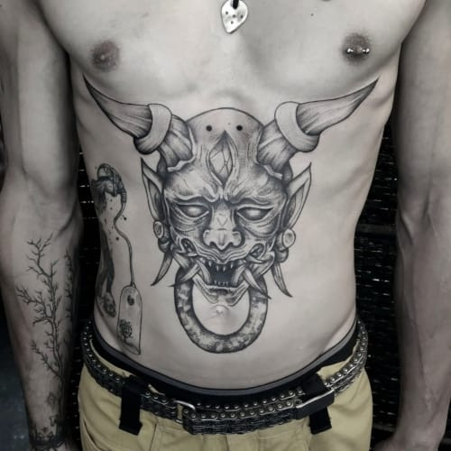 Two demon tattoos on men, one on the arm with a traditional Japanese demon with horns and another on the forearm with a black and grey realistic demon portrait.