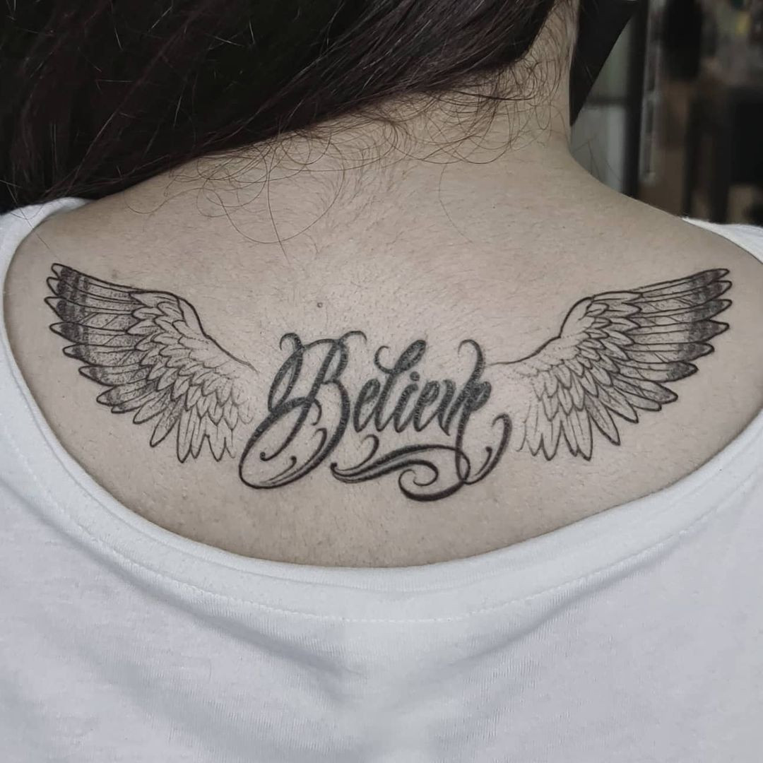 Unique angel wings tattoo for women, featuring the word 'Believe' and a distinctive wing design on the upper back