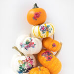 Mini pumpkins decorated with watercolor floral temporary tattoos, displayed as fall decor.