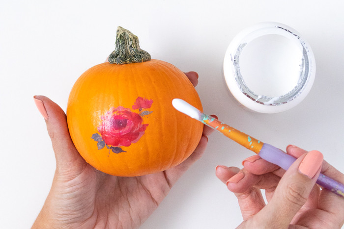 Detailed view of applying a temporary tattoo to a mini pumpkin using a damp sponge, pressing firmly.