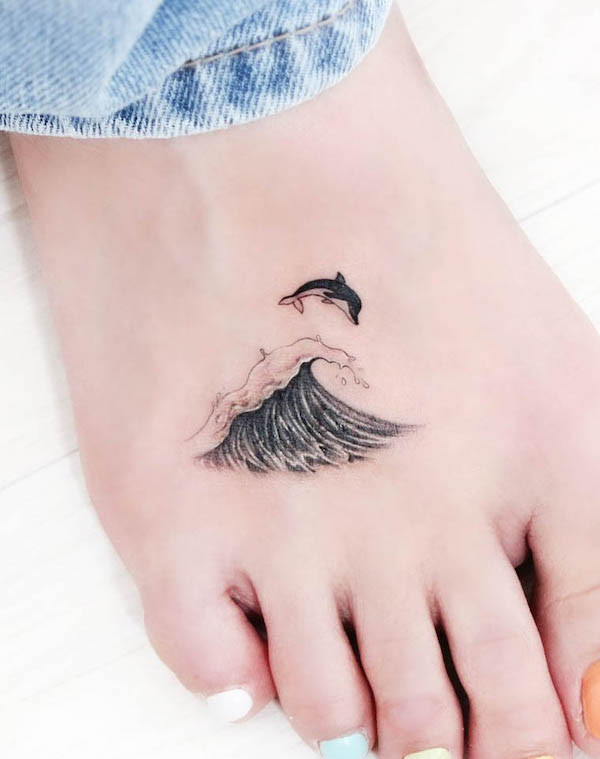 Dolphin and wave foot tattoo, combining symbols of joy, freedom, transformation, and rebirth in a meaningful design