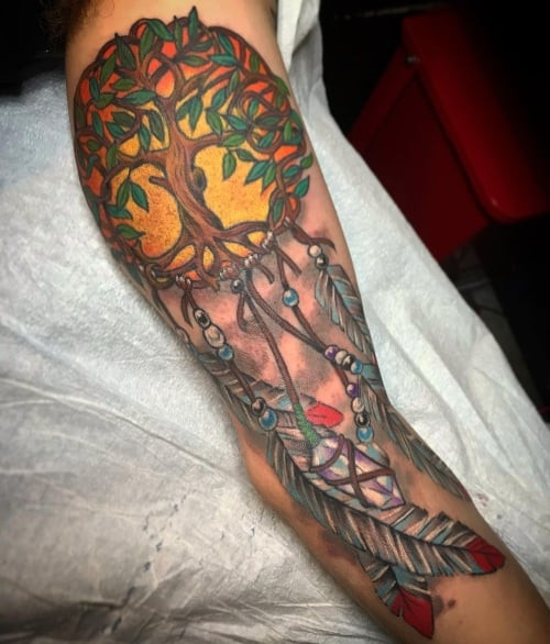 A dreamcatcher tattoo with feathers and beads on a man's arm, symbolizing protection