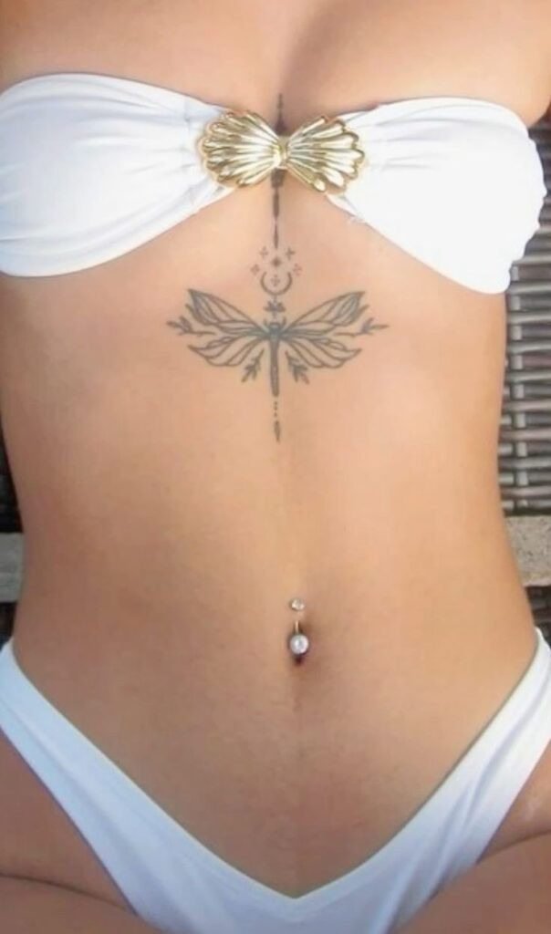 Woman in white bikini with intricate dragonfly tattoo and navel piercing.