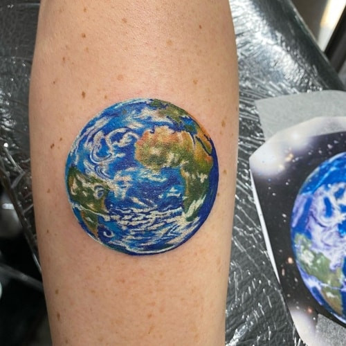 An earth tattoo depicting the globe on a man's shoulder, symbolizing world connection