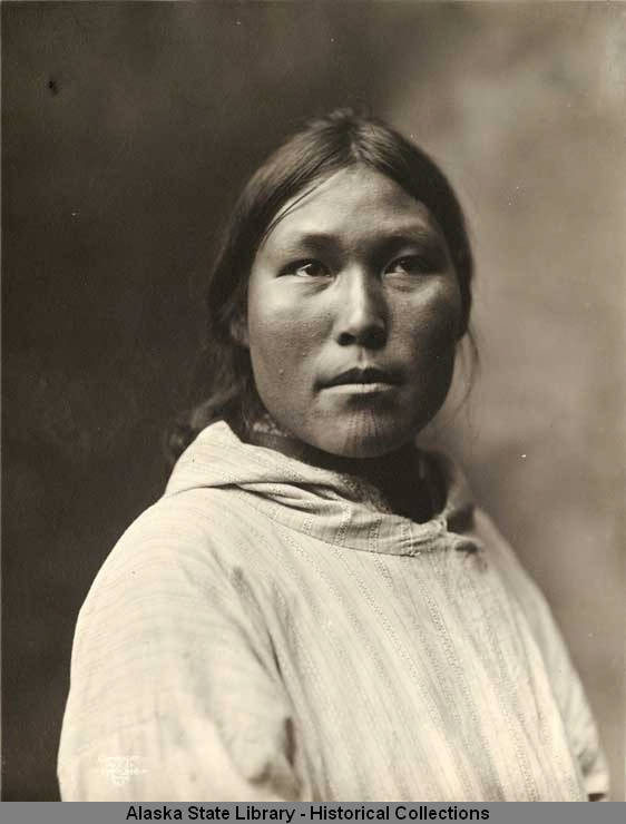 An archival image from 1903 depicts an Inuit woman with traditional facial tattoos, illustrating the historical depth and cultural continuity of Tupik.