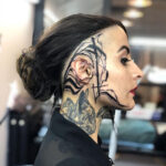 Intricate black ink face tattoo featuring delicate lines and dot work, extending from the temple across the cheekbone.