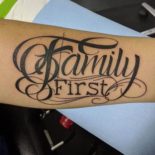 Bold &quot;Family First&quot; script tattoo on a man's forearm, a strong statement family tattoo for men.