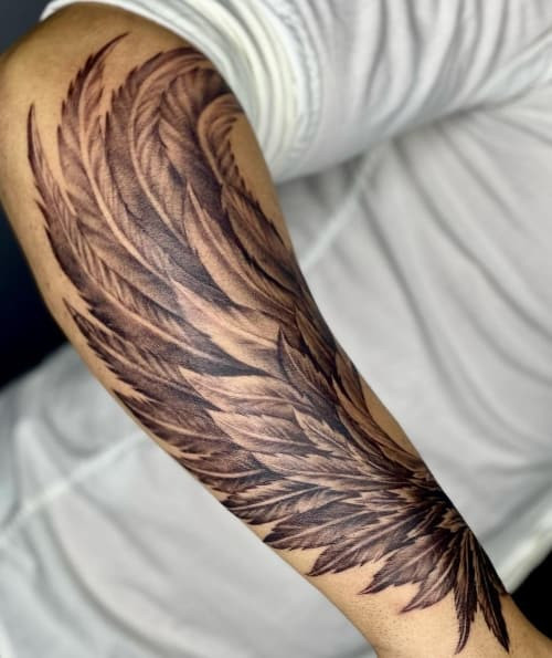 A detailed feather tattoo with intricate barbs on a man's arm, symbolizing freedom and lightness