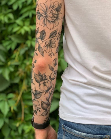 Floral sleeve tattoo for men featuring roses, lilies, and leaves in black and grey ink, wrapping around the arm from shoulder to wrist.