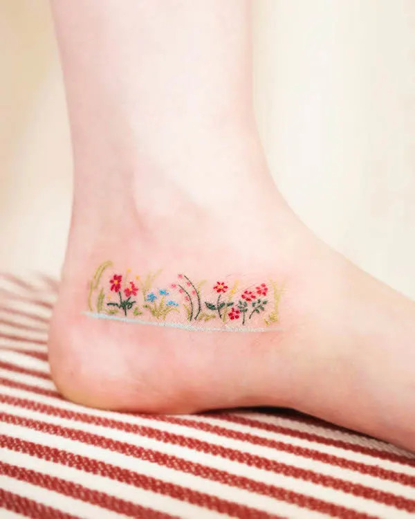 Flower garden ankle tattoo depicting blooming flowers and leaves, creating a vibrant spring garden on the skin