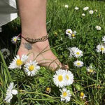 a foot with a dandelion tattoo steps in grass with white flowers