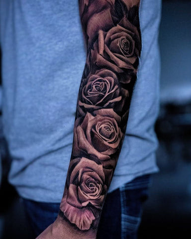 Extensive forearm sleeve tattoo featuring multiple roses in various stages of bloom, interwoven with leaves and thorns for a complete arm design.