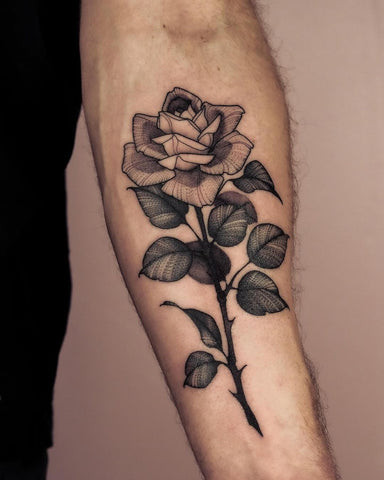 Realistic red rose tattoo on a man's outer forearm, featuring detailed petals, thorns, and shading.