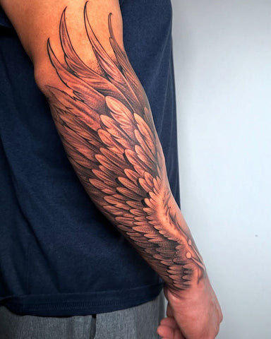 Dramatic black and grey ink forearm sleeve tattoo of a large, detailed angel wing with feathers flowing upwards, symbolizing freedom and spirituality.