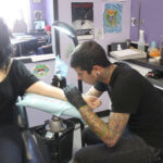 Artist Justin Coppolino tattooing a white ink design.