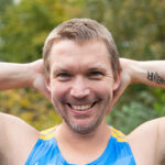 A man in a Gray Nation Endurance race bib has his hands behind his head to show off a tattoo that reads