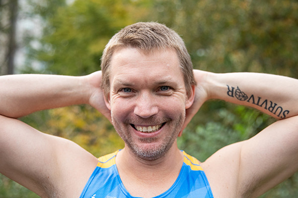 A man in a Gray Nation Endurance race bib has his hands behind his head to show off a tattoo that reads