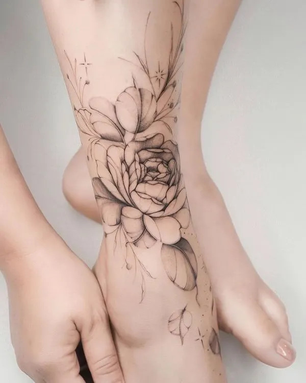 Greyscale flower foot tattoo of a peony, showcasing detailed shading and a 3D effect in black ink