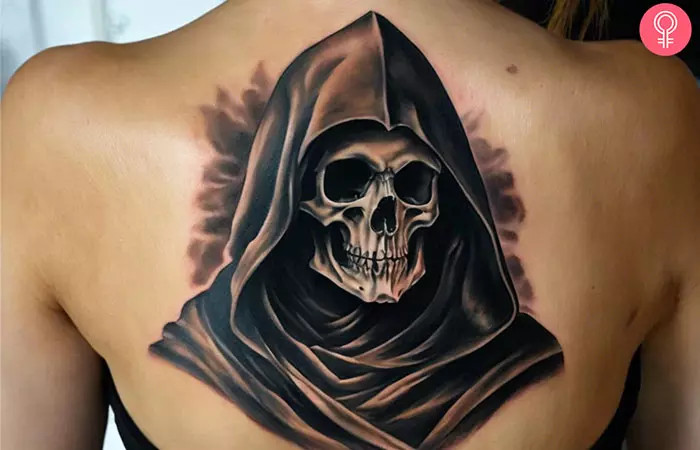 Grim Reaper back tattoo on a woman’s back, etched with precision, featuring dark hollow sockets, haunting gaze, and dark background, representing acceptance of life's mysteries and inevitabilities.