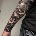 Detailed black and gray half sleeve tattoo of a skull and roses, showcasing intricate shading and realism.