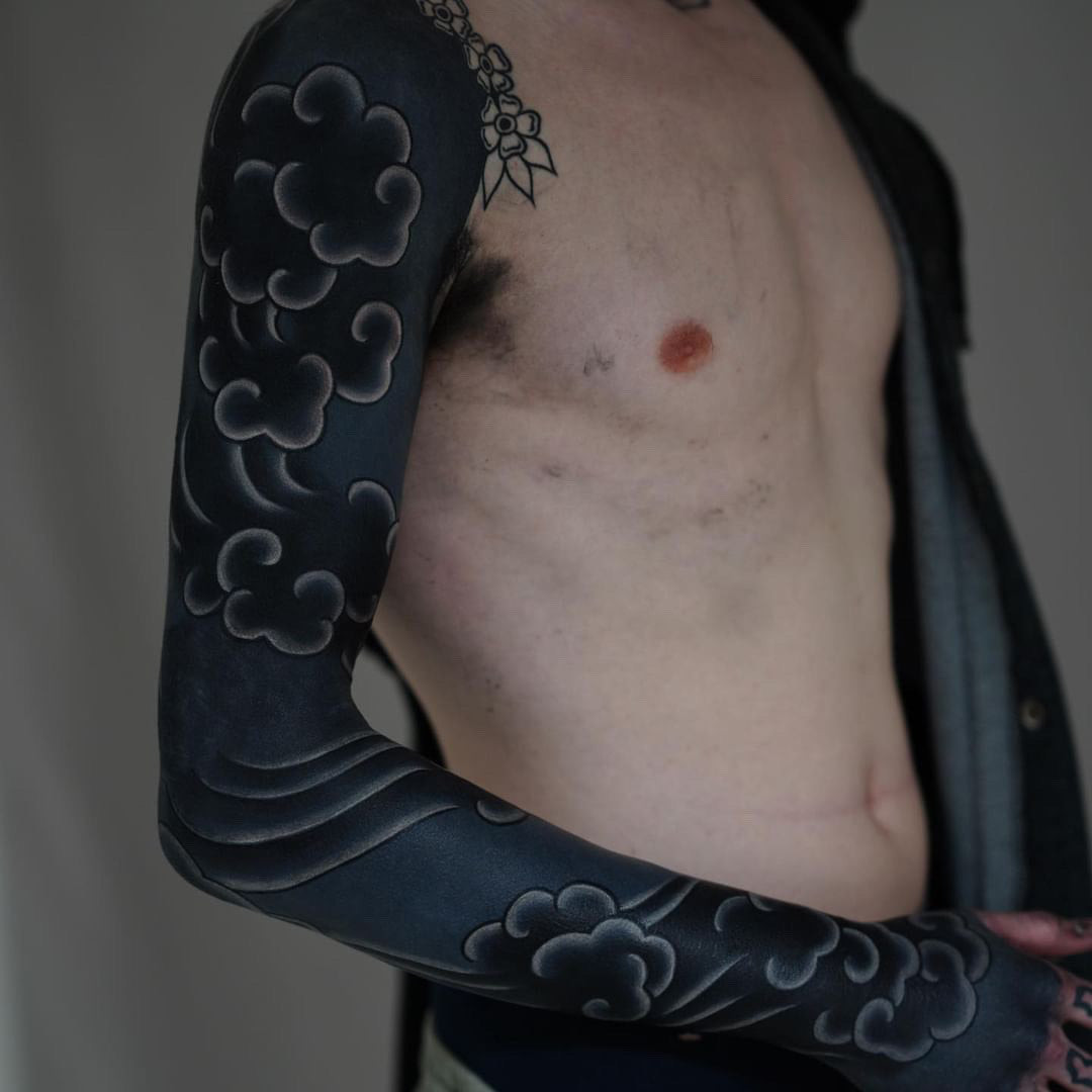 Geometric white ink patterns over a full blackout sleeve tattoo