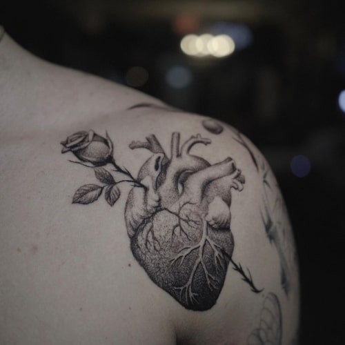 Two heart tattoos on men, one on the forearm with a realistic anatomical heart and another on the arm with a minimalist heart outline.