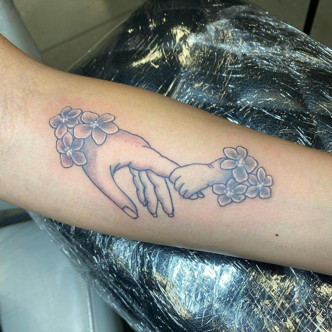 Baby hand holding finger miscarriage tattoo on forearm.