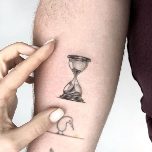 A winged hourglass tattoo on a man's leg, representing fleeting time