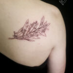 A finely detailed tree branch extending across the shoulder blade, symbolizing growth and strength.