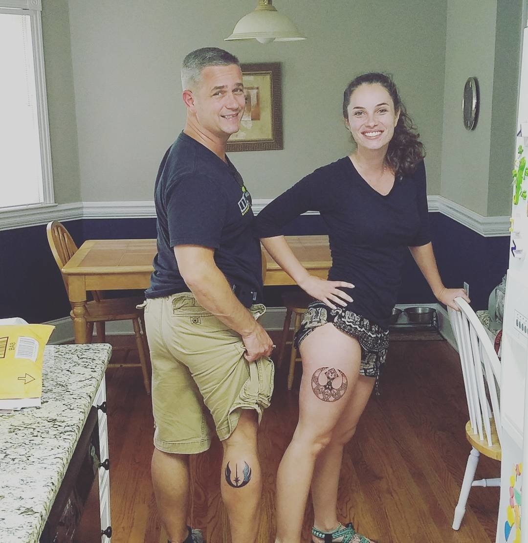 Father and daughter displaying forearm tattoos inspired by Star Wars, featuring contrasting lightsaber designs in red and blue.