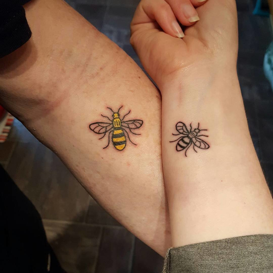 Father and daughter displaying forearm tattoos of bee designs, one larger and one smaller, symbolizing a sweet and industrious bond.