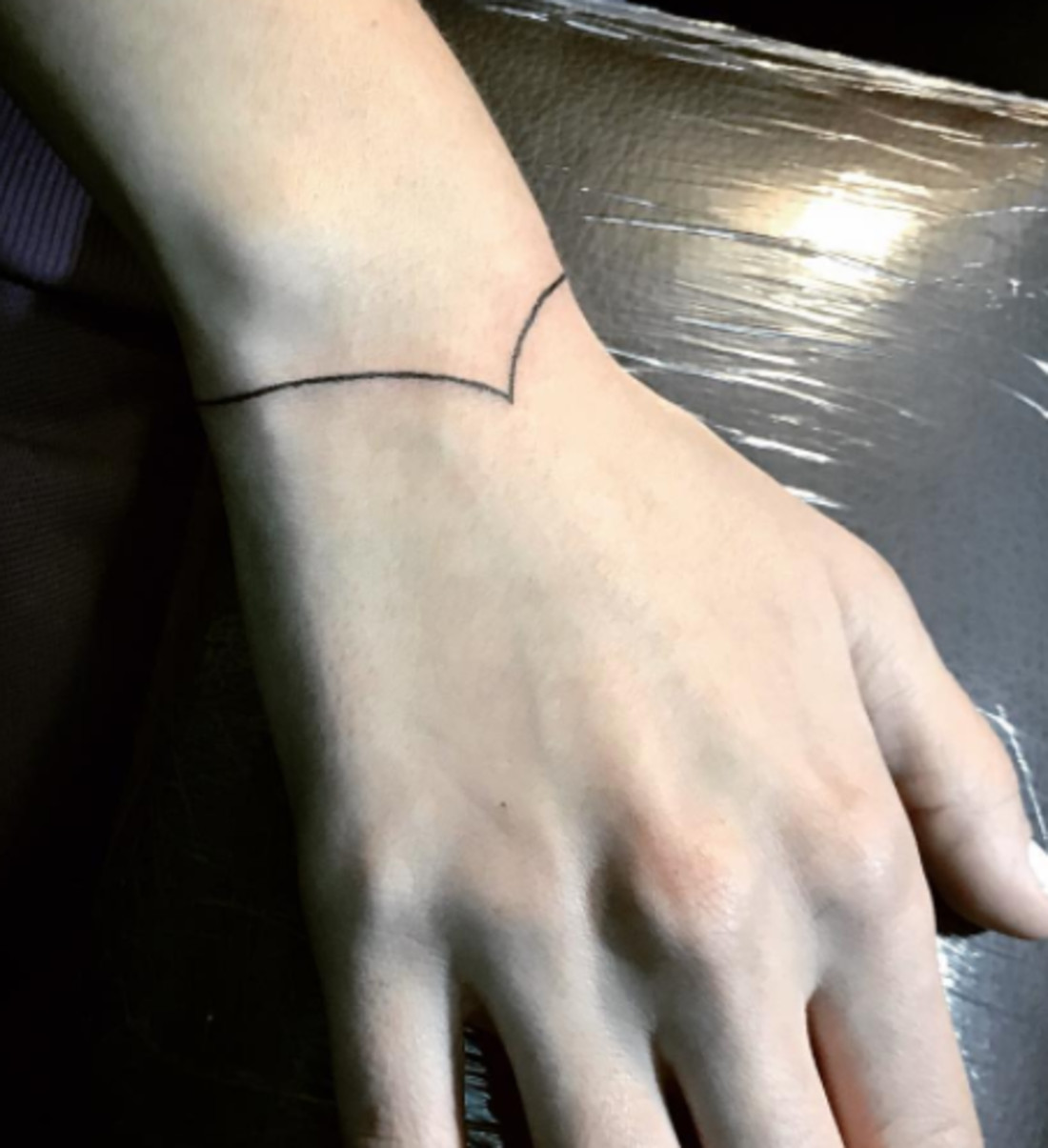 A simple black line tattoo on a wrist, forming a continuous circle.