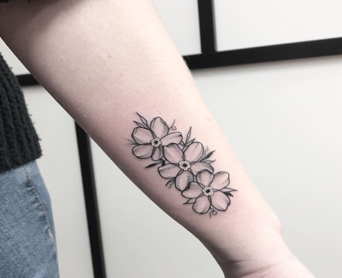 Three small black ink forget-me-not flower tattoos on an outer wrist.