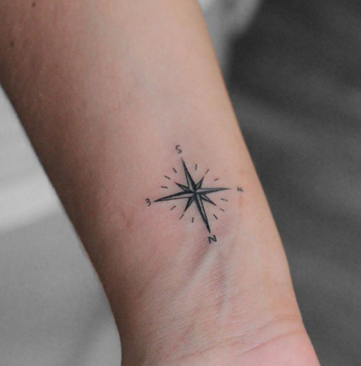 A small and dainty black ink compass tattoo on a wrist.