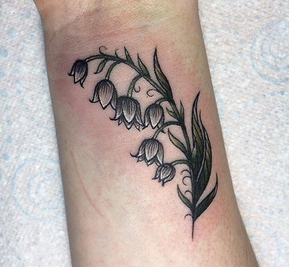 A black ink lily of the valley stem tattoo on a wrist.